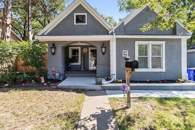 view of front of home featuring stone siding, covered porch, a front lawn, and stucco siding