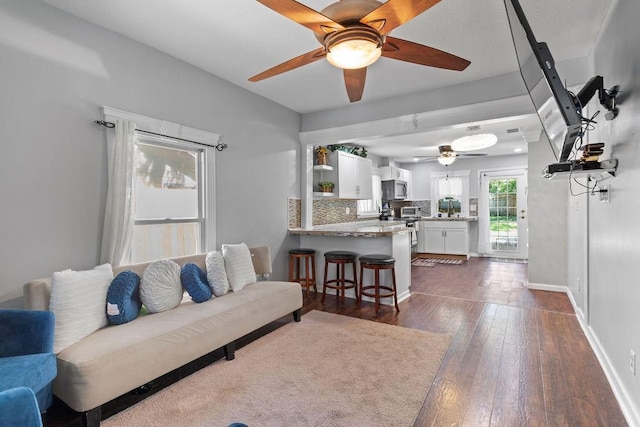 living area featuring ceiling fan, dark wood-type flooring, and baseboards