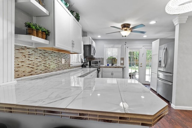 kitchen featuring a peninsula, a sink, white cabinetry, stainless steel refrigerator with ice dispenser, and tasteful backsplash