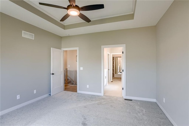 unfurnished bedroom featuring light colored carpet, a tray ceiling, and ceiling fan