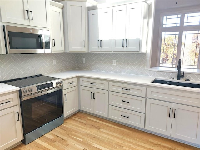 kitchen featuring sink, backsplash, stainless steel appliances, white cabinets, and light hardwood / wood-style flooring