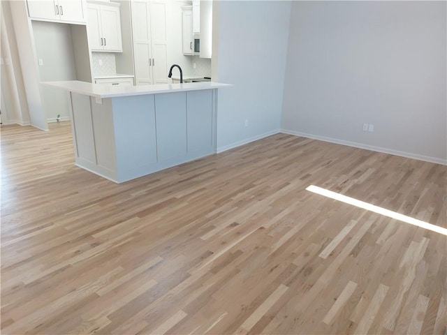 kitchen featuring kitchen peninsula, backsplash, white cabinetry, light hardwood / wood-style floors, and sink