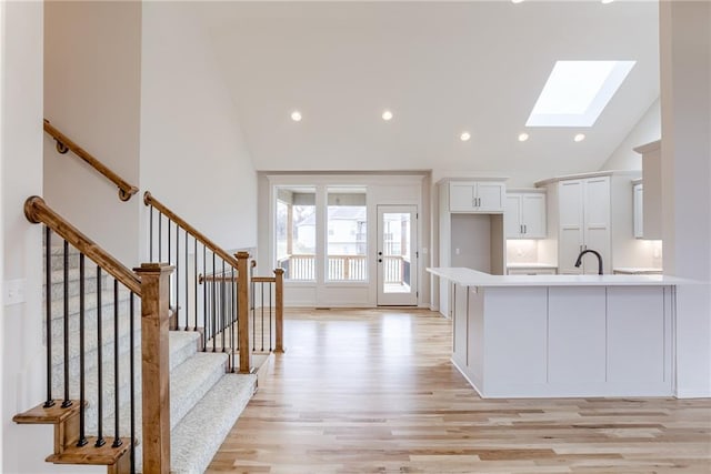 kitchen with white cabinetry, a skylight, high vaulted ceiling, kitchen peninsula, and light hardwood / wood-style floors