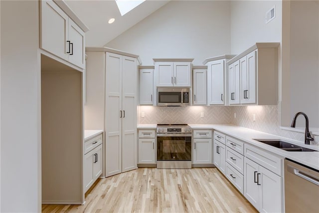 kitchen featuring sink, appliances with stainless steel finishes, white cabinets, decorative backsplash, and light wood-type flooring