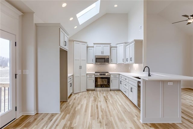 kitchen with sink, light hardwood / wood-style flooring, appliances with stainless steel finishes, kitchen peninsula, and backsplash