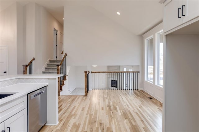 kitchen featuring white cabinetry, dishwasher, vaulted ceiling, and light hardwood / wood-style flooring