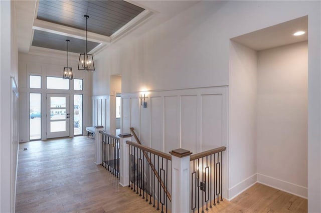 hall featuring an inviting chandelier, a raised ceiling, and light wood-type flooring