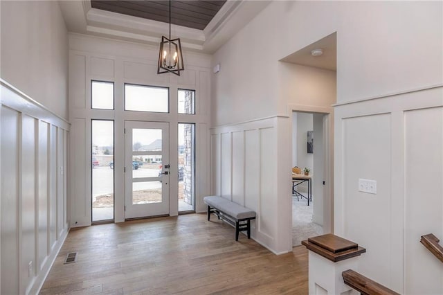 entrance foyer featuring a high ceiling, a raised ceiling, a notable chandelier, and light hardwood / wood-style floors