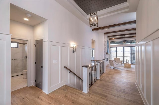 corridor with beamed ceiling, a chandelier, and light hardwood / wood-style flooring