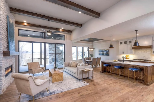 living room with sink, beam ceiling, a fireplace, and light hardwood / wood-style floors