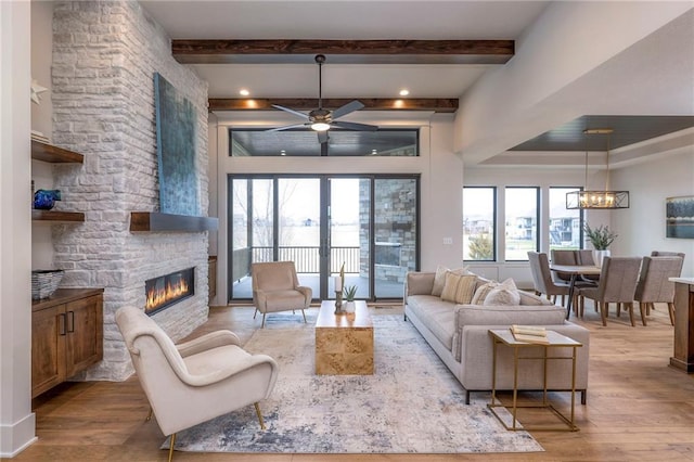 living room featuring a stone fireplace, ceiling fan with notable chandelier, beamed ceiling, light hardwood / wood-style floors, and french doors