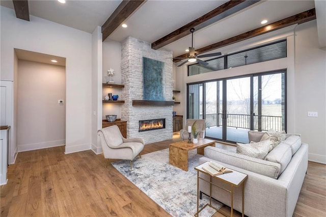 living room with french doors, a stone fireplace, light hardwood / wood-style flooring, ceiling fan, and beam ceiling