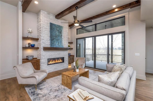 living room with a stone fireplace, light hardwood / wood-style flooring, french doors, and beamed ceiling