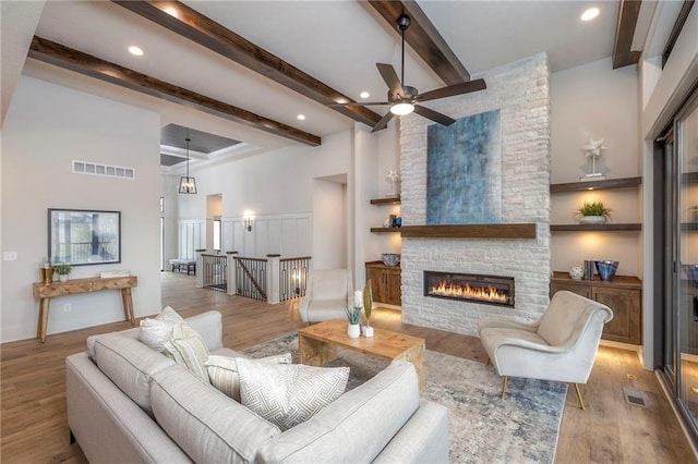 living room with a towering ceiling, a fireplace, beam ceiling, and light wood-type flooring