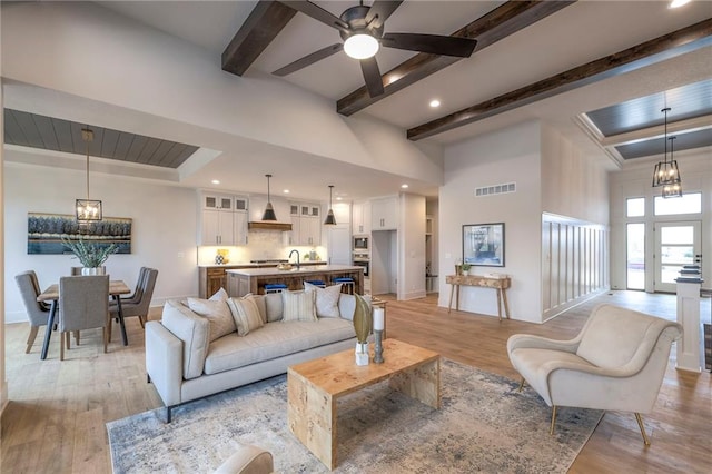 living room with beamed ceiling, sink, ceiling fan with notable chandelier, and light hardwood / wood-style floors