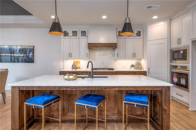 kitchen with white cabinetry, light stone countertops, oven, and a center island with sink