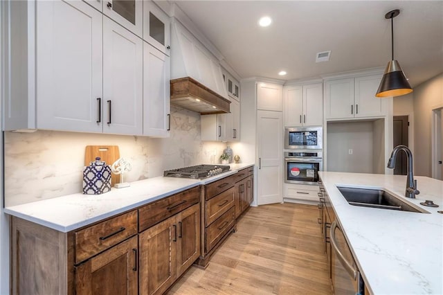 kitchen with decorative light fixtures, white cabinetry, sink, stainless steel appliances, and light stone countertops