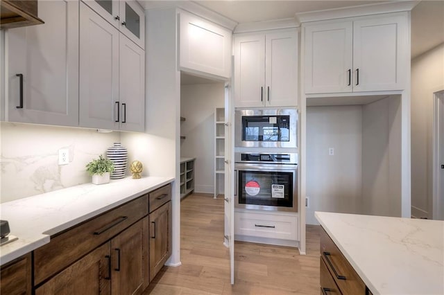 kitchen featuring white cabinetry, stainless steel oven, light stone countertops, and light hardwood / wood-style flooring