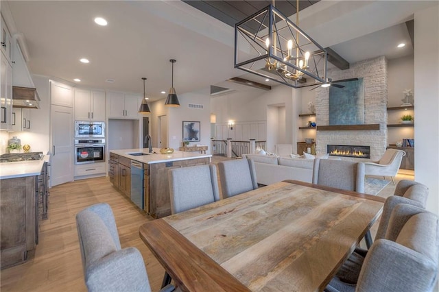 dining space with a stone fireplace, sink, light hardwood / wood-style flooring, and a notable chandelier