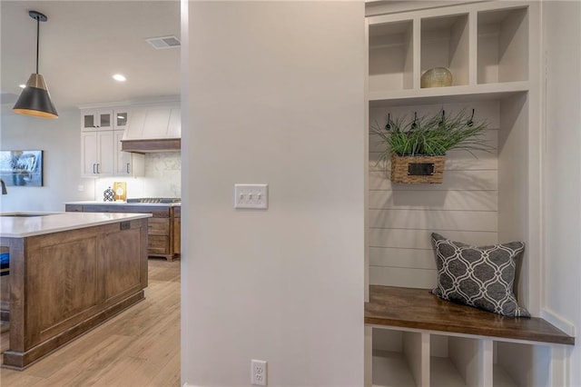 kitchen with light hardwood / wood-style flooring, decorative backsplash, custom range hood, white cabinets, and decorative light fixtures