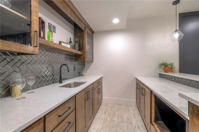 kitchen featuring light stone counters, sink, decorative light fixtures, and backsplash