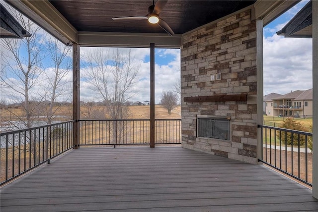 deck with ceiling fan and an outdoor stone fireplace