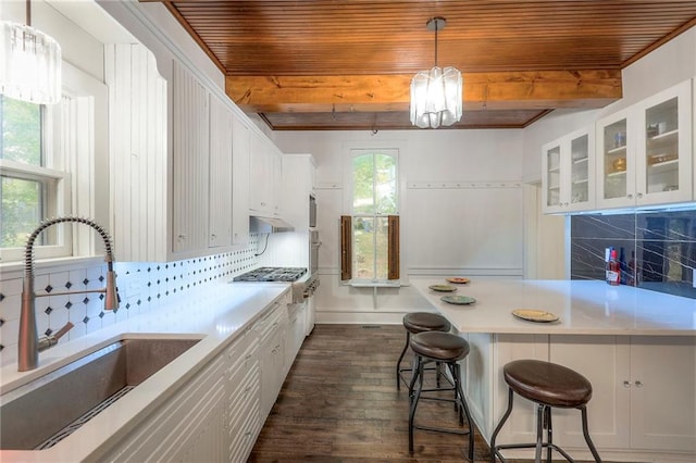 kitchen with decorative backsplash, light countertops, a sink, and beam ceiling