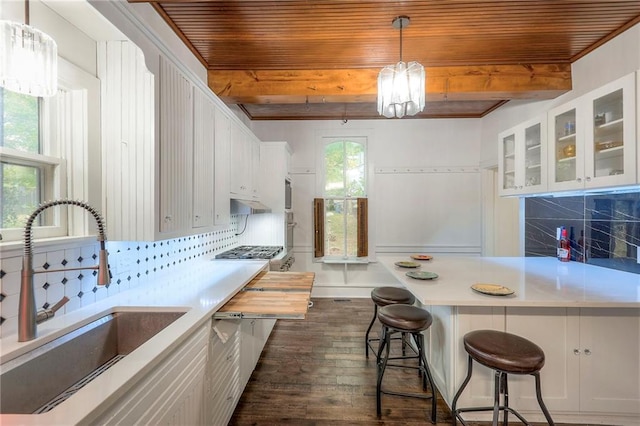 kitchen with beamed ceiling, light countertops, decorative backsplash, and a sink