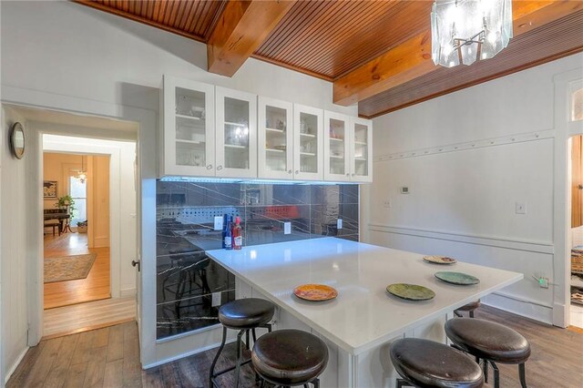 kitchen featuring white cabinetry, tasteful backsplash, a breakfast bar, beam ceiling, and wood finished floors