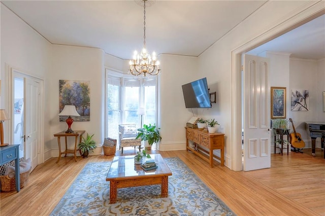 living area featuring light wood finished floors, crown molding, baseboards, and a chandelier