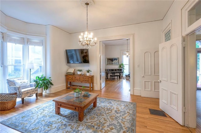 living room with visible vents, light wood-type flooring, a notable chandelier, and plenty of natural light