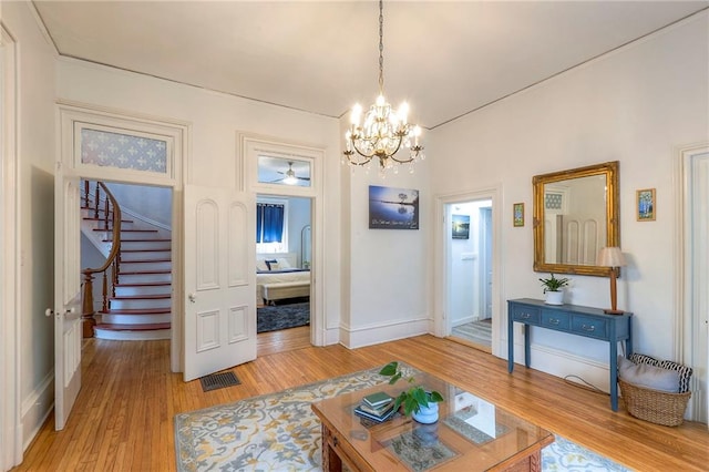 living area with visible vents, baseboards, stairs, light wood-type flooring, and ceiling fan with notable chandelier
