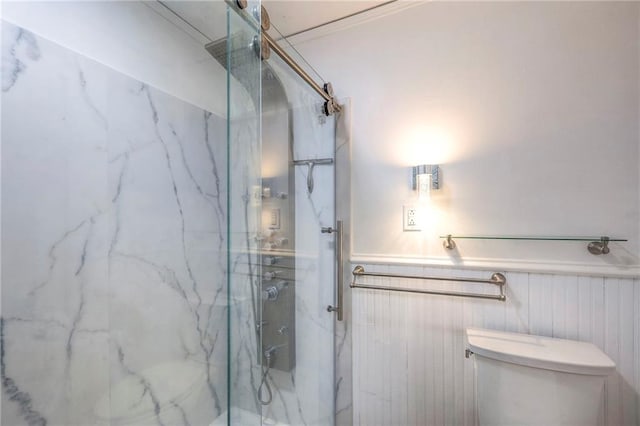 bathroom with a wainscoted wall, toilet, and a marble finish shower