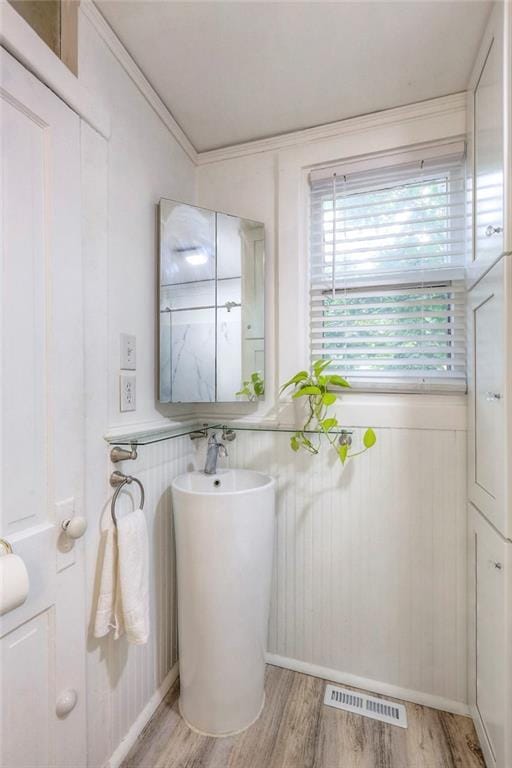 bathroom featuring wood finished floors, ornamental molding, and visible vents