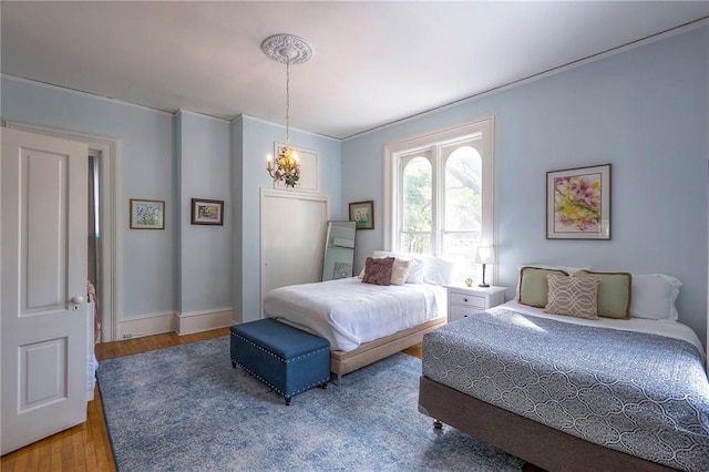 bedroom featuring baseboards, wood finished floors, ornamental molding, and a chandelier