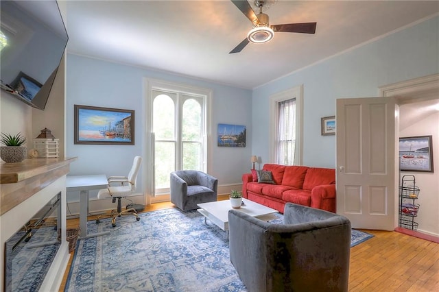 living room featuring baseboards, light wood-style flooring, ceiling fan, and ornamental molding