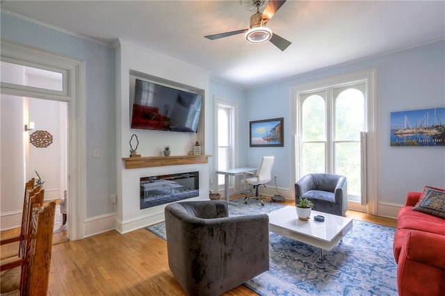 living room with a ceiling fan, crown molding, light wood-style floors, and a glass covered fireplace