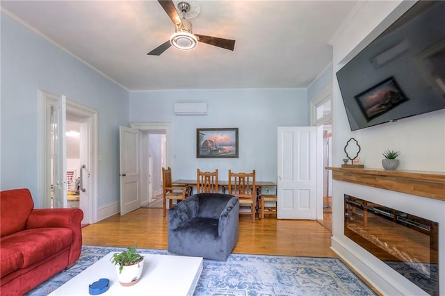 living room with ornamental molding, ceiling fan, a glass covered fireplace, a wall mounted air conditioner, and wood finished floors