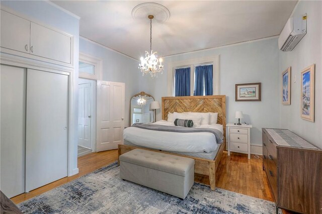 bedroom featuring a notable chandelier, crown molding, wood finished floors, and an AC wall unit
