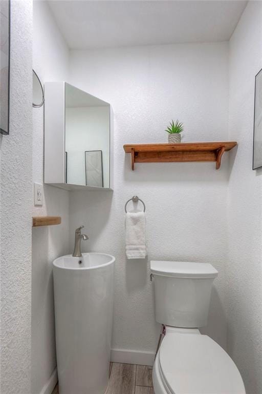 half bathroom with baseboards, toilet, and wood finished floors