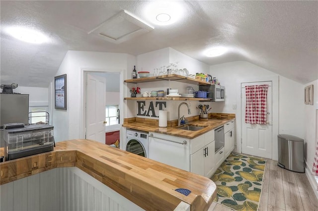 kitchen with butcher block countertops, a textured ceiling, a sink, and washer / dryer