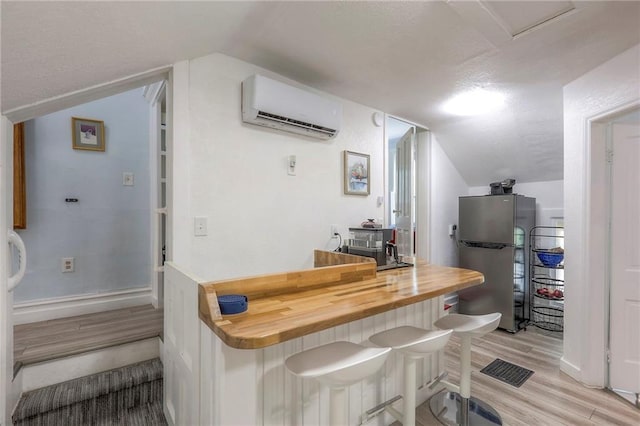 bar with light wood finished floors, baseboards, vaulted ceiling, an AC wall unit, and freestanding refrigerator