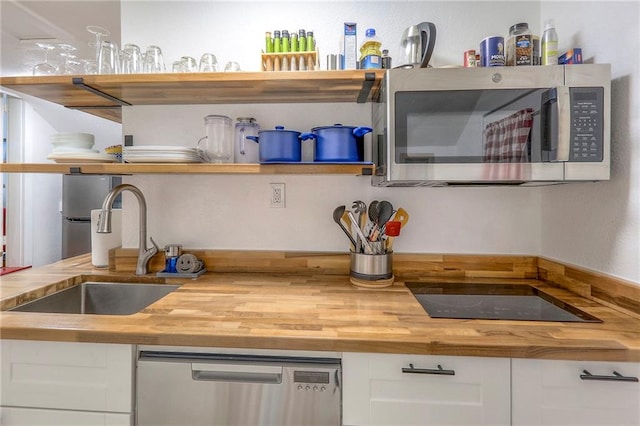 kitchen with white cabinetry, open shelves, butcher block countertops, a sink, and appliances with stainless steel finishes