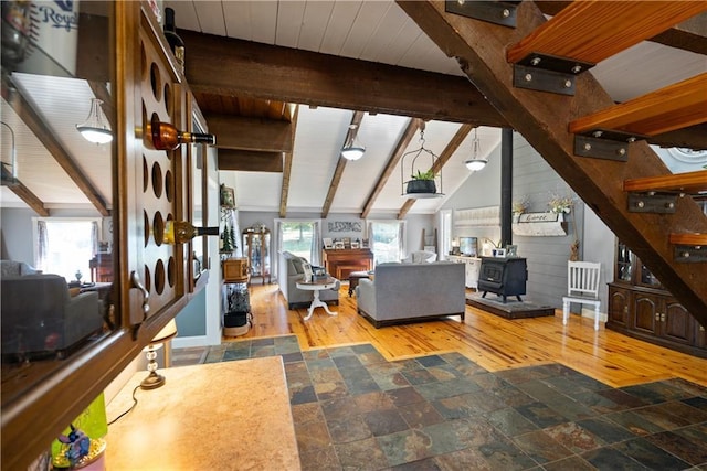 living room with vaulted ceiling with beams, hardwood / wood-style flooring, a wealth of natural light, and a wood stove