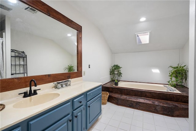 bathroom with vanity, vaulted ceiling with skylight, tile patterned flooring, and tiled tub