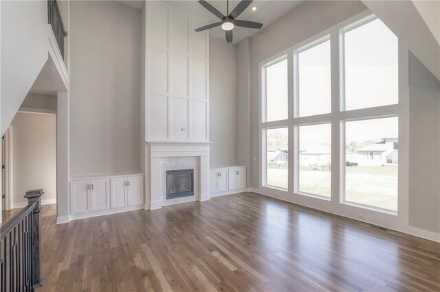 unfurnished living room with baseboards, a towering ceiling, ceiling fan, dark wood-type flooring, and a fireplace