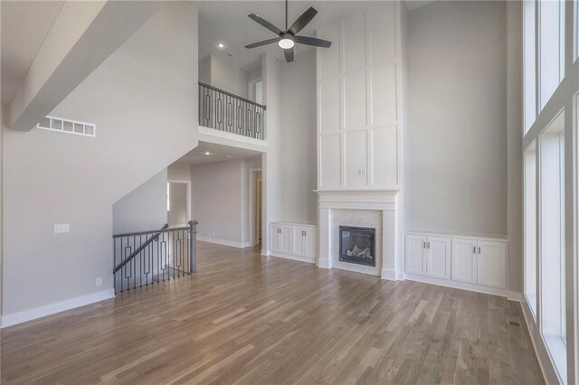 unfurnished living room featuring a fireplace, wood finished floors, a towering ceiling, visible vents, and baseboards