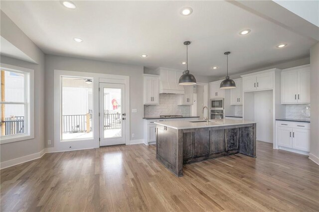 kitchen with appliances with stainless steel finishes, white cabinetry, hanging light fixtures, and premium range hood