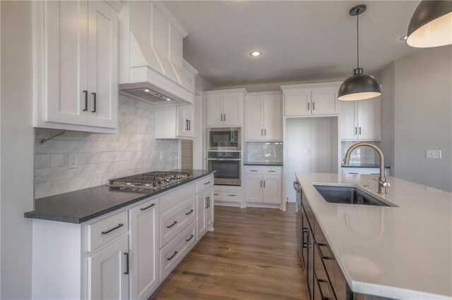 kitchen with stainless steel appliances, white cabinets, premium range hood, and a sink