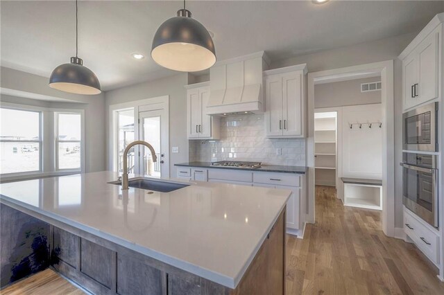 kitchen featuring appliances with stainless steel finishes, white cabinets, a sink, and pendant lighting